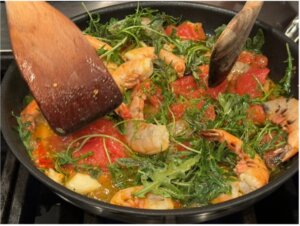 Preparing the sauce with shrimp with arugula, tomato, orange juice, and cream.